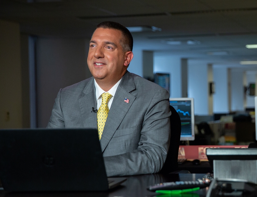 Paul Aversano smiling at his desk with an American flag lapel pin